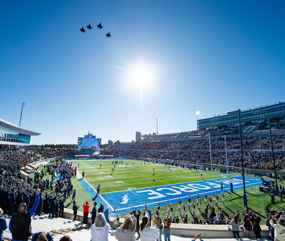 A color photograph of a military flyover above the Air Force Academy football stadium on a sunny day.