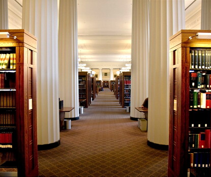 A color photograph of the hallway of Harvard Law School's library, flanked on either side by columns and bookshelves.