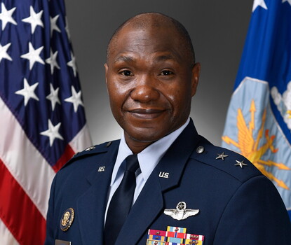 A color photograph of Rodney Lewis, a Black man, in Air Force dress uniform with decoration ribbons on his left breast and the American flag behind him.