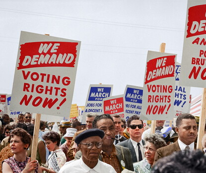  A color photograph of Black and white men and women holding red and white and blue and white signs in support of civil rights.