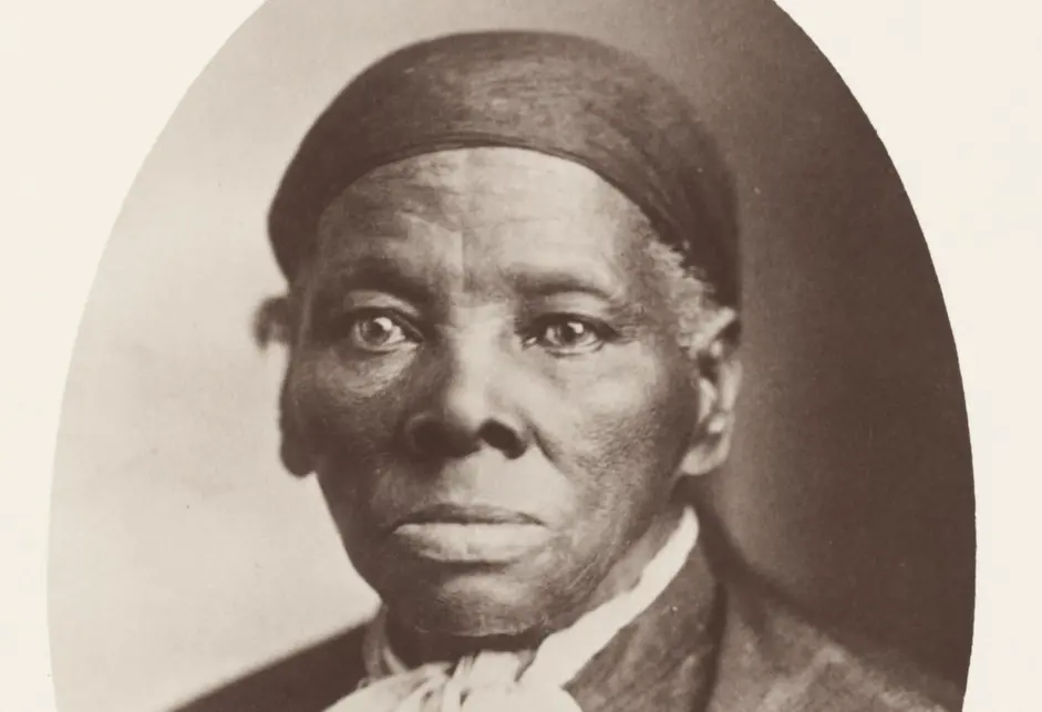 Harriet Tubman, a Black woman, wearing a dark headscarf covering her gray hair, a white scarf, and a dark jacket.