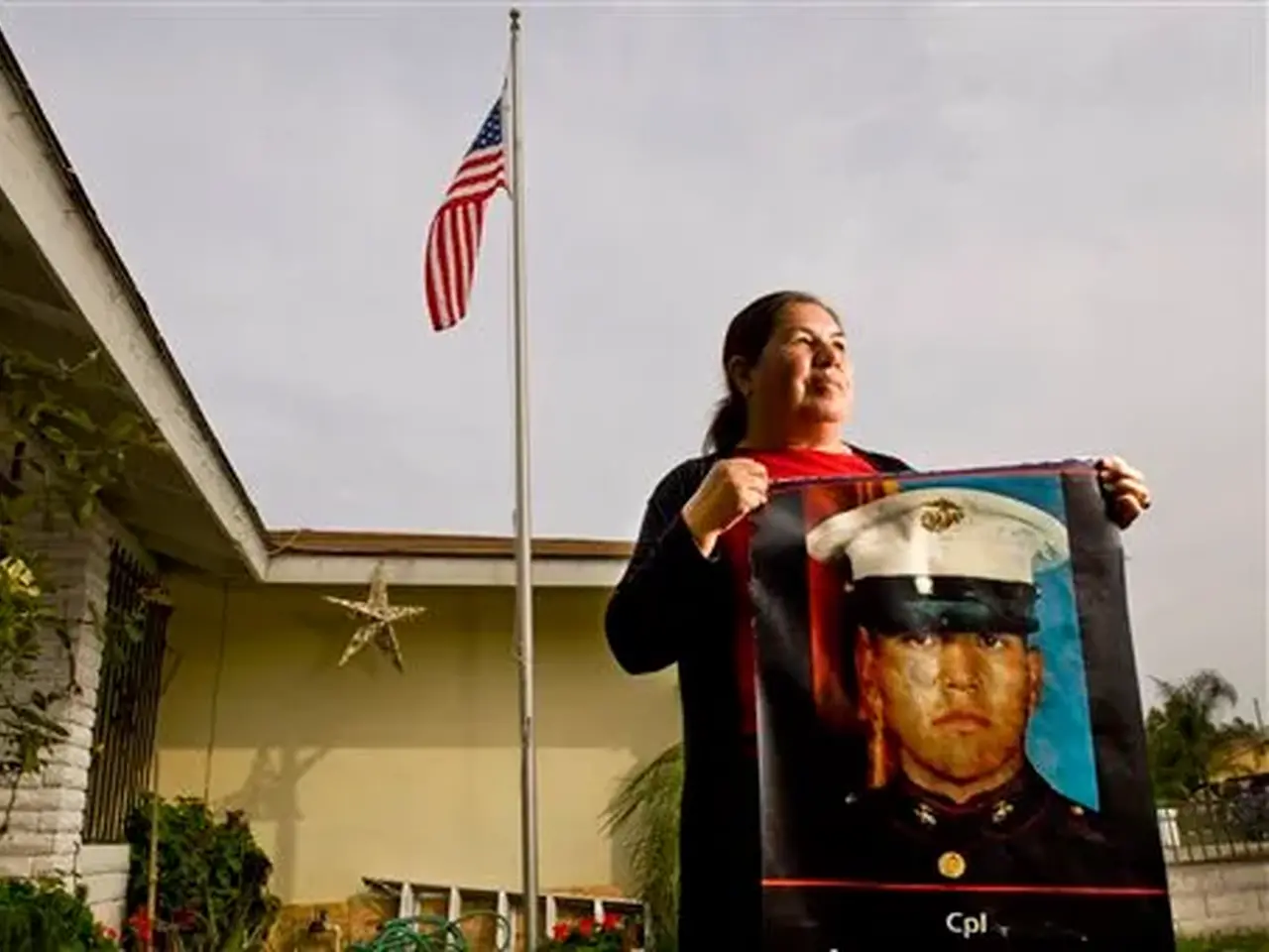 Photograph of Simona Garibay holding a banner of her son in front of US flag