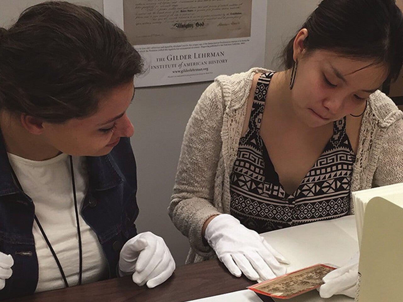 Two Gilder Lehrman Interns working at the Collection, examining a historical photograph while wearing white gloves