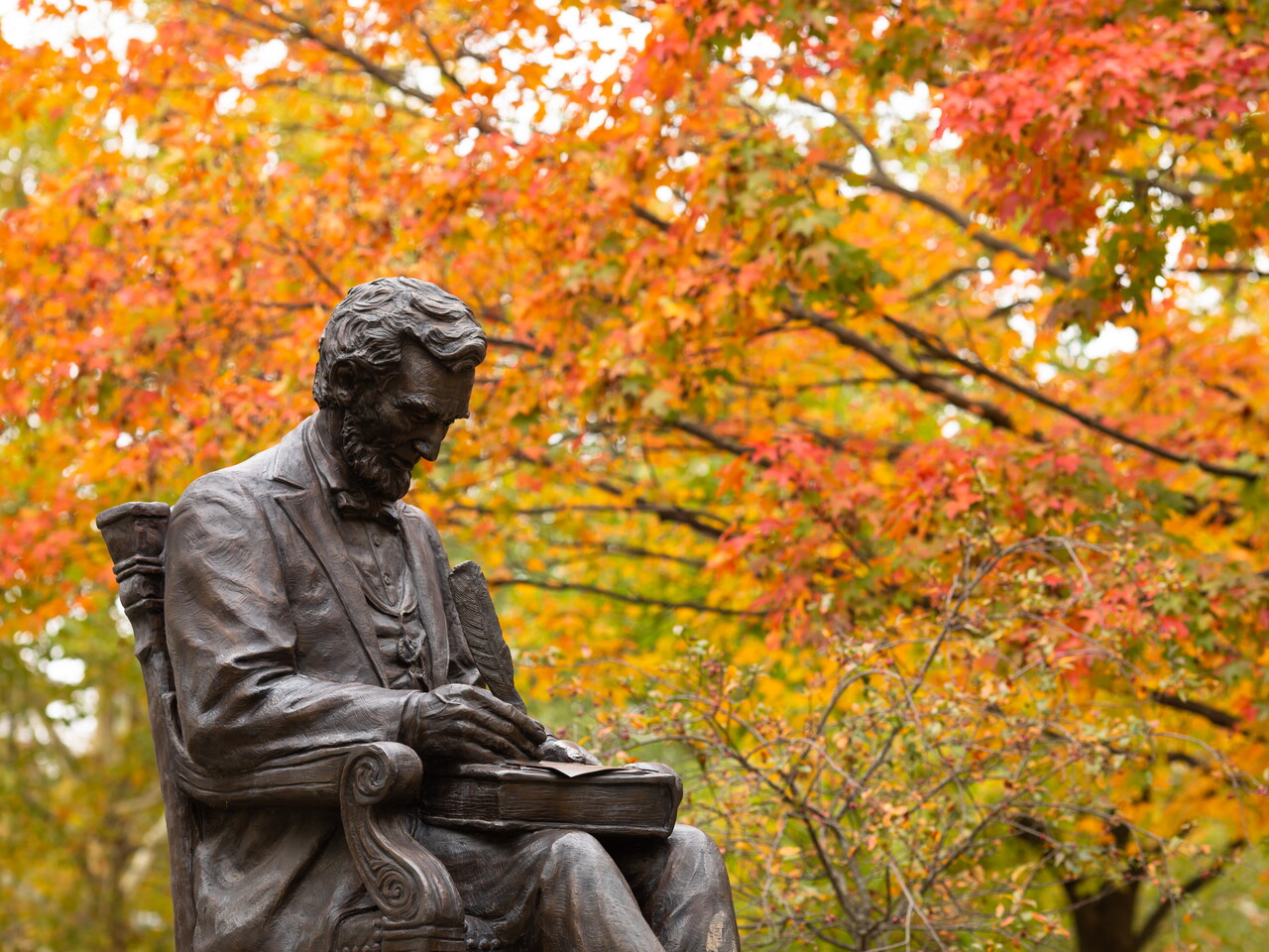 Photograph taken during autumn, showing statue of Lincoln with quill in hand, on Gettysburg campus, fall folliage in background