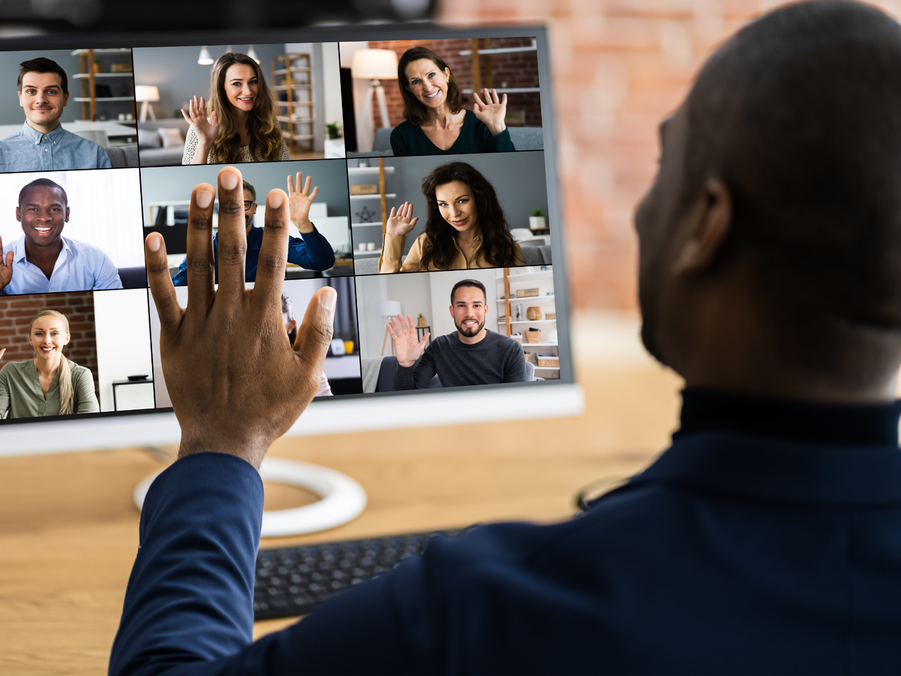 Man waving at computer with zoom session live and attendees waving back