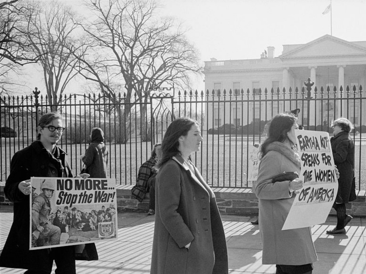 A photograph of anti-Vietnam War demonstrators carrying signs, "No more...Stop the war!", "Eartha Kitt speaks for the women of America", and "Stop the draft", picketing in front of the White House.