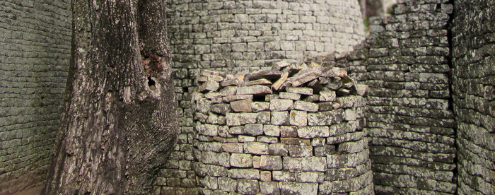 A round stone tower next to a tree, flanked on all sides by stone walls