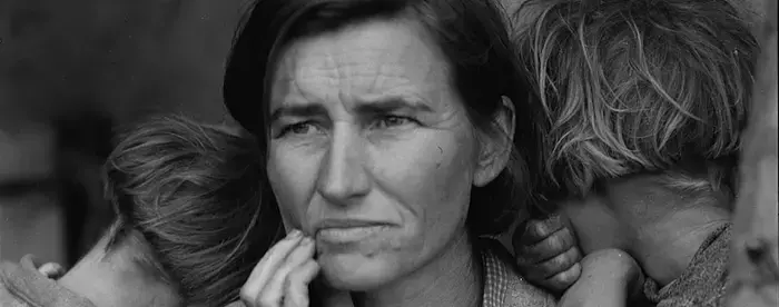 A destitute migrant mother with her children, one in her lap and two leaning against her shoulders. 