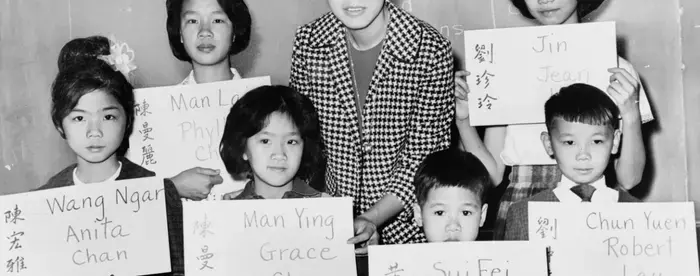 April Lou, teacher at PS 1, Manhattan, with six Chinese children, recent arrivals from Hong Kong and Formosa, who are holding up placards giving his or her Chinese name in ideographs and in transliteration. Photo by Fred Palumbo, 1964 (Library of Congress)