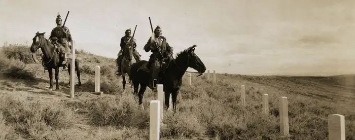 Hillside with cemetery and three Native American men on horseback.
