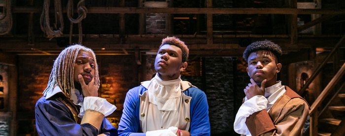 Three students at a Hamilton performance, dressed in revolutionary garbs, looking thoughtful