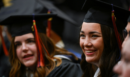 View of two graduating MA program students in cap and gown (one in the foreground, the other in the background) at the inaugural Gettysburg Commencement Ceremony