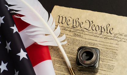 A quill laying across the Constitution