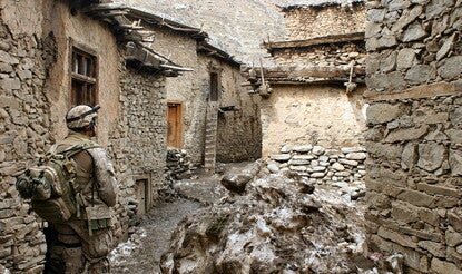 Soldier walking through alley between houses in desert terrain