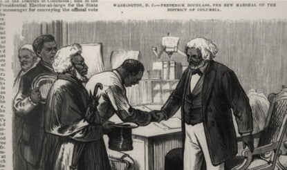 An engraving of a white-haired Frederick Douglass standing at a desk, wearing a dark jacket and waistcoat, dark bow tie, and white shirt and pants, shaking the hand of another Black man as other people wait to greet him at left