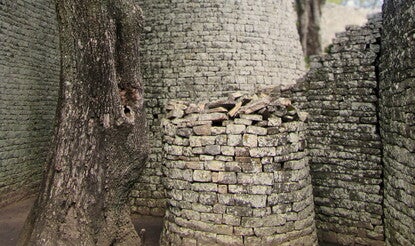 A round stone tower next to a tree, flanked on all sides by stone walls