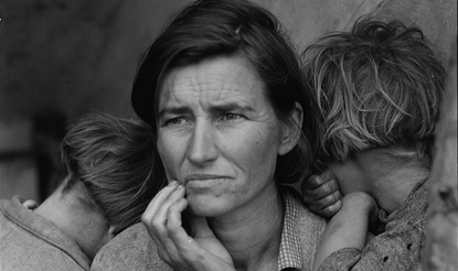 A destitute migrant mother with her children, one in her lap and two leaning against her shoulders. 