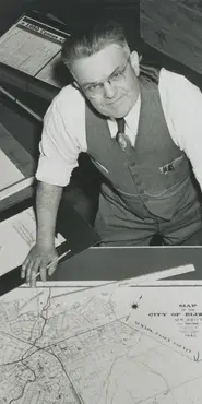 Photograph of census supervisor standing over a map.