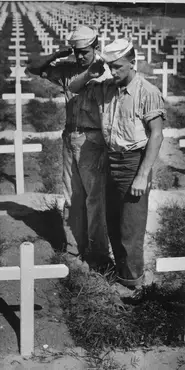Black and white photograph showing two soldiers saluting a grave in a cemetery.