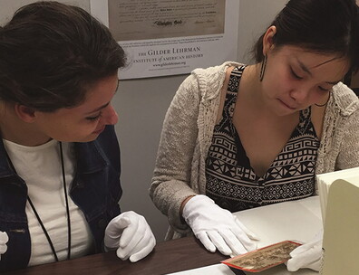 Two Gilder Lehrman Interns working at the Collection, examining a historical photograph while wearing white gloves