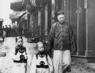 Black and white photograph of Chinese man and two children walking down a street