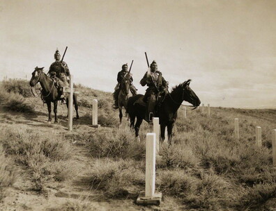 Hillside with cemetery and three Native American men on horseback.