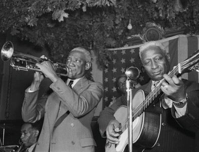 Musicians playing a guitar and the trumpet perform in front of an American flag