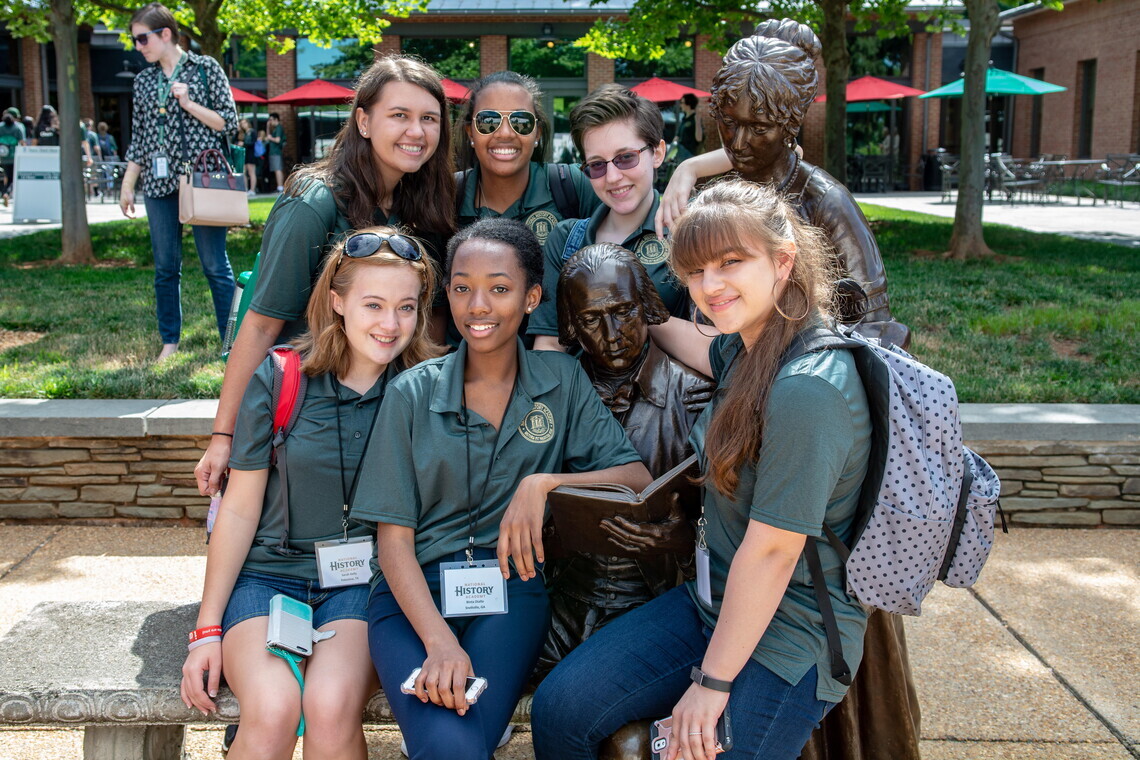 A group of seven students from the National History Academy in green uniforms posed around a bronze statue