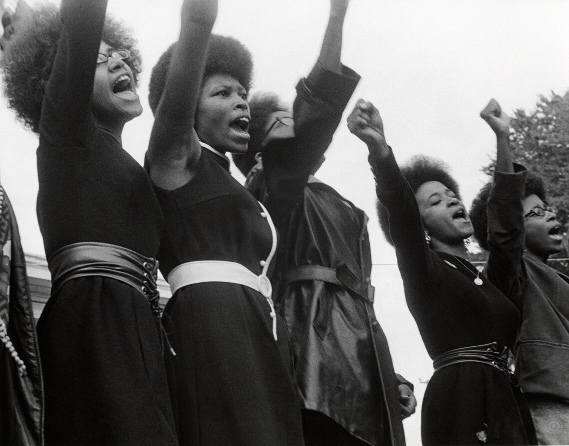 Seven Black women with Afros raising their right fists.