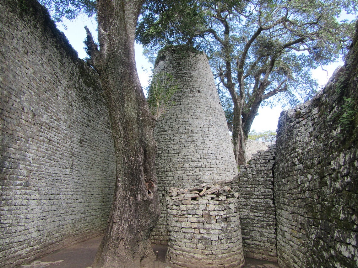 A round stone tower next to a tree, flanked on all sides by stone wall