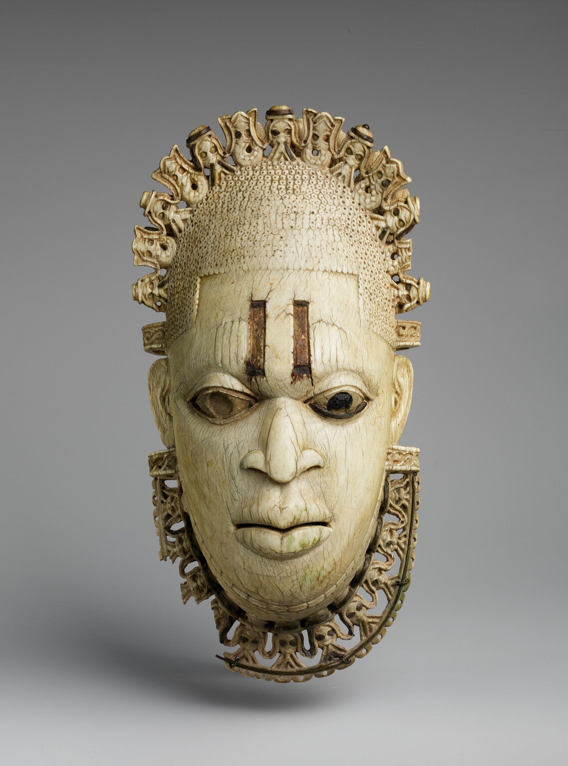 An ivory and metal mask of a woman, with a tiara and necklace