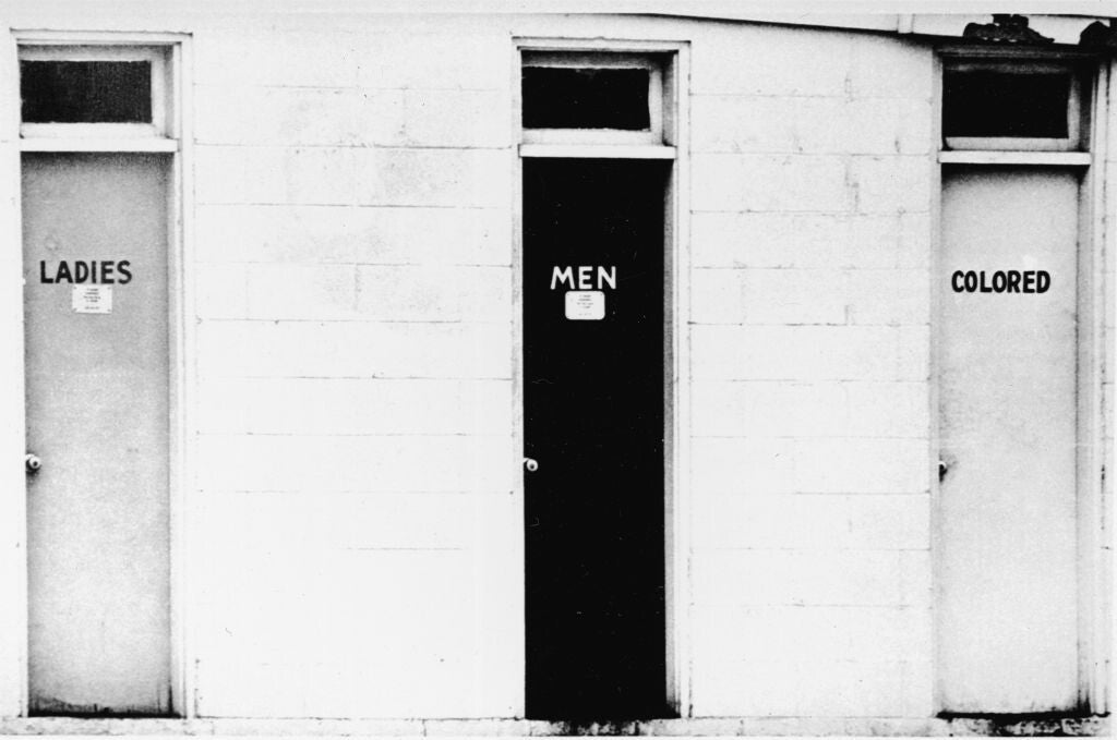 Three bathroom doors in a cement-block building labeled, from left to right, "Ladies," "Men," and "Colored."