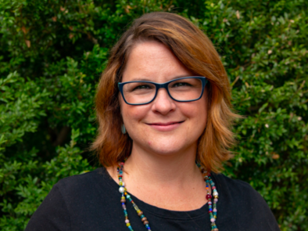 a bespectacled white woman wearing a black shirt and a double-stranded necklace.