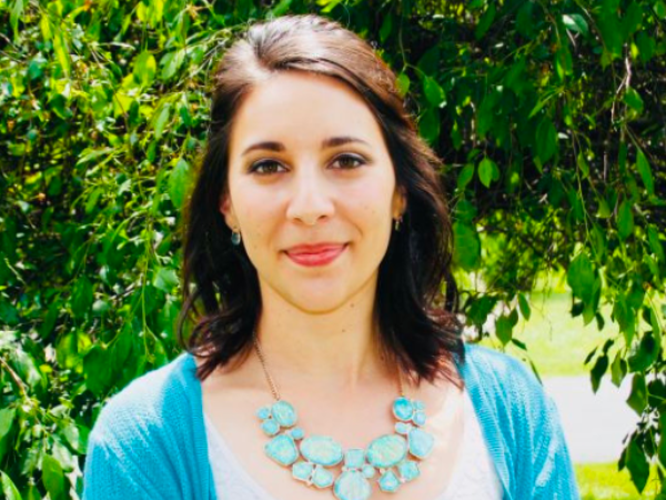 a white woman wearing a light blue cardigan and necklace and a white shirt.