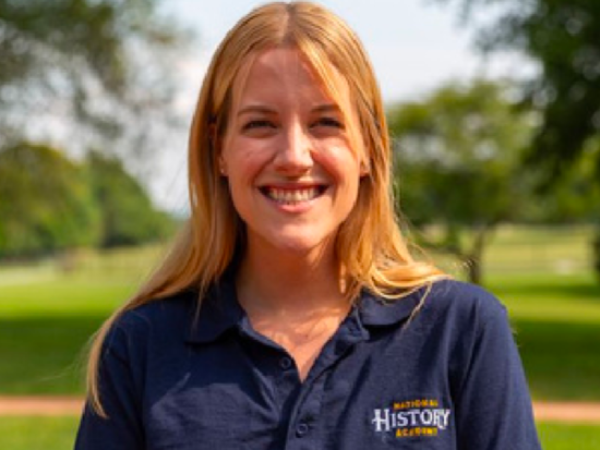 a white woman smiling while wearing a blue polo shirt emblazoned with the National History Academy wordmark.