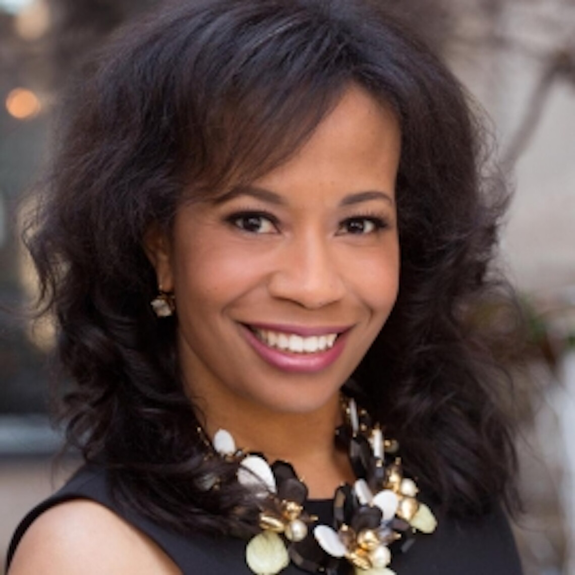 A Black woman with dark hair and a metallic necklace smiling.
