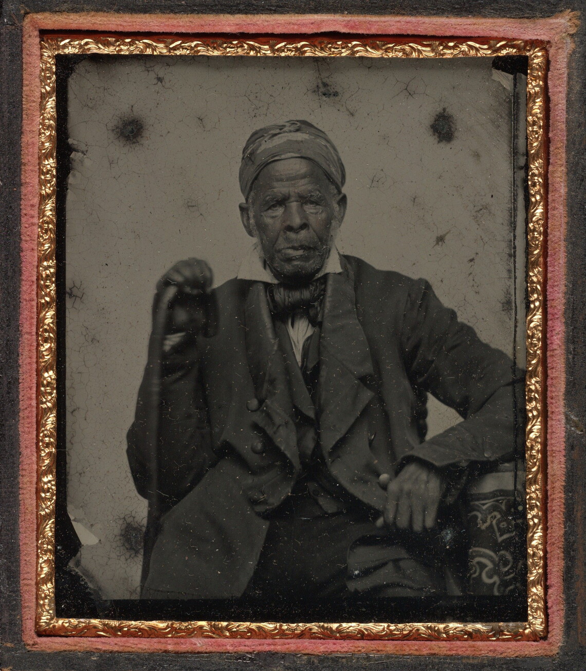 A black-and-white photograph of Omar Ibn Said, a Black man holding a cane in his right hand and wearing a turban, jacket, coat, tie, and a white shirt.
