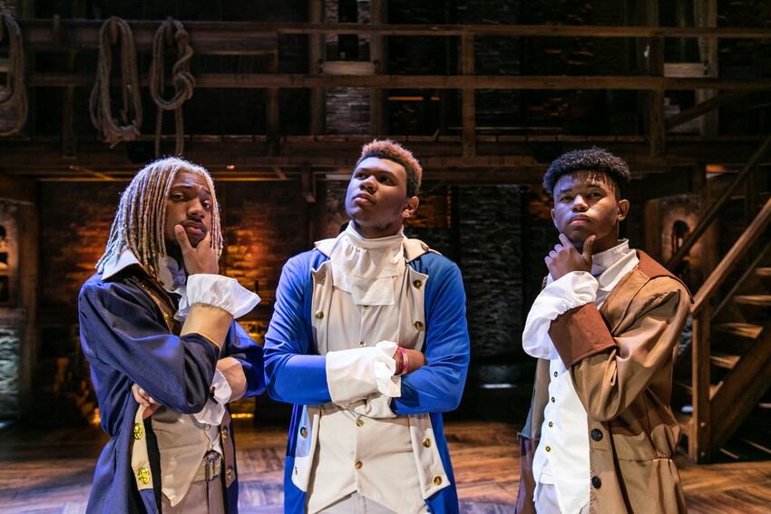 Three students at a Hamilton performance, dressed in revolutionary garbs, looking thoughtful