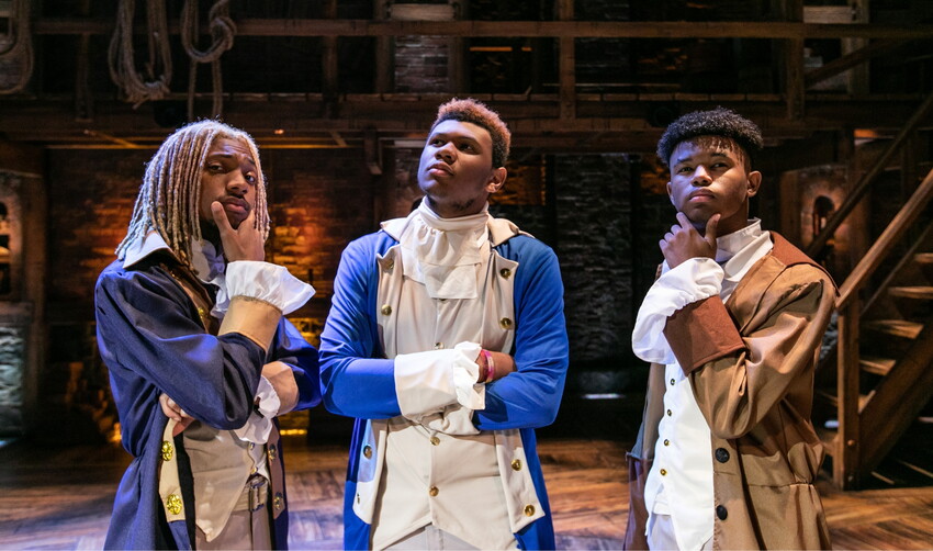 Three students at a Hamilton performance, dressed in revolutionary garbs, looking thoughtful